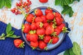 fresh juicy strawberries in a blue plate on an old wooden rural table, next to it is a dark blue napkin and mint leaves and