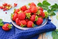 fresh juicy strawberries in a plate on an old wooden rural table, next to it is a dark blue napkin and currant berries Royalty Free Stock Photo