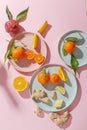 Fresh juicy tangerines, pomegranates and sliced fruits on colored plates on a pink background. Summer mood, healthy food. Top view