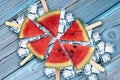 Fresh, juicy and tasty slices of watermelon on ice and a blue wooden surface.