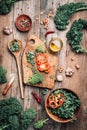 Fresh kale in bowl, wooden spoon, fork, chopping board, spices, salt, garlic, pepper on rustic wooden background. Top view. Copy Royalty Free Stock Photo