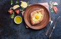 Fresh khachapuri with wholegrain flour, cottage cheese, egg, sulugini cheese, vegetables, butter, greens, plate, fork