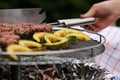 fresh kofta lamb meat spits and seasoned pumpking slices are grilled by a woman on a stainless steel charcoal grill