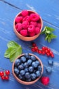 Fresh, large blueberries and raspberries in a wooden bowl close-up with mint stamens on a blue wooden background. Royalty Free Stock Photo