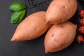 Fresh large pink sweet potato tubers with tomatoes and spices on a dark background Royalty Free Stock Photo