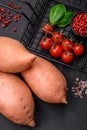 Fresh large pink sweet potato tubers with tomatoes and spices on a dark background Royalty Free Stock Photo