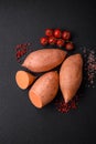 Fresh large pink sweet potato tubers with tomatoes and spices on a dark background Royalty Free Stock Photo