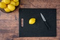 Fresh lemon on a black cutting board, wood table, basket of lemons, paring knife