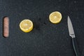 Fresh lemon cut in half on a black cutting board, paring knife