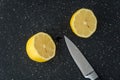 Fresh lemon cut in half on a black cutting board, paring knife