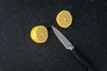 Fresh lemon cut in half on a black cutting board, paring knife