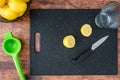 Fresh lemon cut in half on a black cutting board, paring knife, wood table, basket of lemons, citrus squeezer, glass