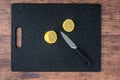 Fresh lemon cut in half on a black cutting board, paring knife, wood table