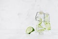 Fresh lemonades with green cucumber, soda water, ice cubes in transparent yoke bottles on soft light white wood table, copy space.