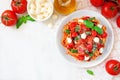 Linguine pasta with tomatoes, mozzarella and basil, top view corner border over white marble