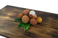 Fresh lychee and peeled showing the red skin and white flesh with green leaf on a wooden background. Lychi with leaves - tropical