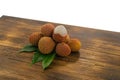 Fresh lychee and peeled showing the red skin and white flesh with green leaf on a wooden background. Lychi with leaves - tropical