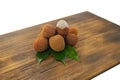 Fresh lychee and peeled showing the red skin and white flesh with green leaf on a wooden background. Lychi with leaves - tropical
