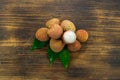 Fresh lychee and peeled showing the red skin and white flesh with green leaf on a wooden background. Lychi with leaves - tropical