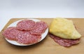 Fresh made salami sandwich, with slices of salami in a white dish, on wooden table and white background Royalty Free Stock Photo