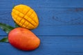 Fresh mango, beautiful chopped fruit with green leaves on dark wooden table background. Tropical fruit design concept. Flat lay.