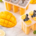 Fresh mango fruit popsicle ice in the plastic shaping box on bright marble table. Summer mood concept product design, close up