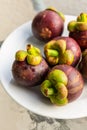 Fresh mangosteen whole fruit lies on a white plate close-up vertical photo