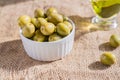 Fresh marinated green olives in white ceramic bowl and sauceboat of premium virgin olive oil on burlap cloth background