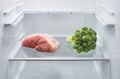 Fresh meat and broccoli opposite each other in an empty refrigerator