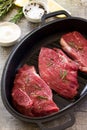 Fresh meat. Raw steak beef on a cast-iron grill frying pan, olive oil, spices and fresh rosemary on the kitchen table Royalty Free Stock Photo
