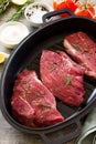 Fresh meat. Raw steak beef on a cast-iron grill frying pan, tomatoes, olive oil, spices and fresh rosemary on the kitchen table Royalty Free Stock Photo