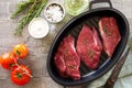 Fresh meat. Raw steak beef on a cast-iron grill frying pan, tomatoes, olive oil, spices and fresh rosemary on the kitchen table. Royalty Free Stock Photo