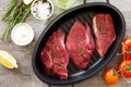 Fresh meat. Raw steak beef on a cast-iron grill frying pan, tomatoes, olive oil, spices and fresh rosemary on the kitchen table. Royalty Free Stock Photo