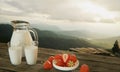 Fresh milk in a clear glass and pitcher. Bright red strawberry in a white ceramic cup. Plank flooring for the table. The mountain