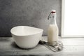 Fresh milk,cream bottle, bowl and wire whisk on window sill