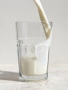 Fresh milk pouring into a glass staying on light marble table Royalty Free Stock Photo