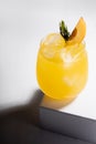 Fresh misted shine orange alcohol cocktail in glass with ice, green rosemary twig, peach slice on podium in sunlight with shadows. Royalty Free Stock Photo