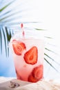 Fresh misted strawberry cocktail on tropical beach in sun glares with sea view and palm leaves, vertical. Summer drink on hot. Royalty Free Stock Photo