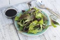 Fresh mixed green salad in round plate, rustic white wooden background. Healthy food, diet concept Royalty Free Stock Photo