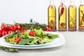 Fresh mixed salad with cherry tomatoes on white plate. Bottles of olive oil with spices and herbs Royalty Free Stock Photo