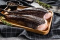 Fresh monkfish without a head on a wooden tray with a cleaver. Gray background. Top view