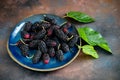 Fresh mulberry with leaves on blue ceramic plate on grunge rusty metal background. Close-up. Selective focus