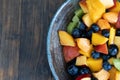 Colorful fresh fruit salad in dark bowl on wooden table in daytime Royalty Free Stock Photo