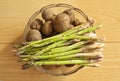 Fresh new potatoes and green asparagus in a glass bowl. Top view close up image on wooden background Royalty Free Stock Photo