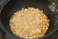 Fresh onion slices fryng in boiling oil in black kazan cauldron, closeup view.