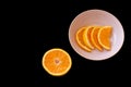 Fresh orange for breakfast with a black background. the fruit is in little slices in a pink plates