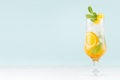 Fresh orange cocktail with slices fruits, mint, straw, ice cubes in misted glass on white wood table and blue color wall.