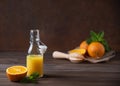 Fresh orange juice in bottle with citrus fruits and mint on a brown wooden background. Healthy and diet drink. Front view and