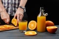 Fresh orange juice in a glass and bottle with fresh fruits sliced with a knife. Man cuts oranges at the wooden table Royalty Free Stock Photo