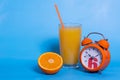 Fresh orange juice in a glass, fruit cut in half, orange alarm clock isolated on a blue background, copy space Royalty Free Stock Photo